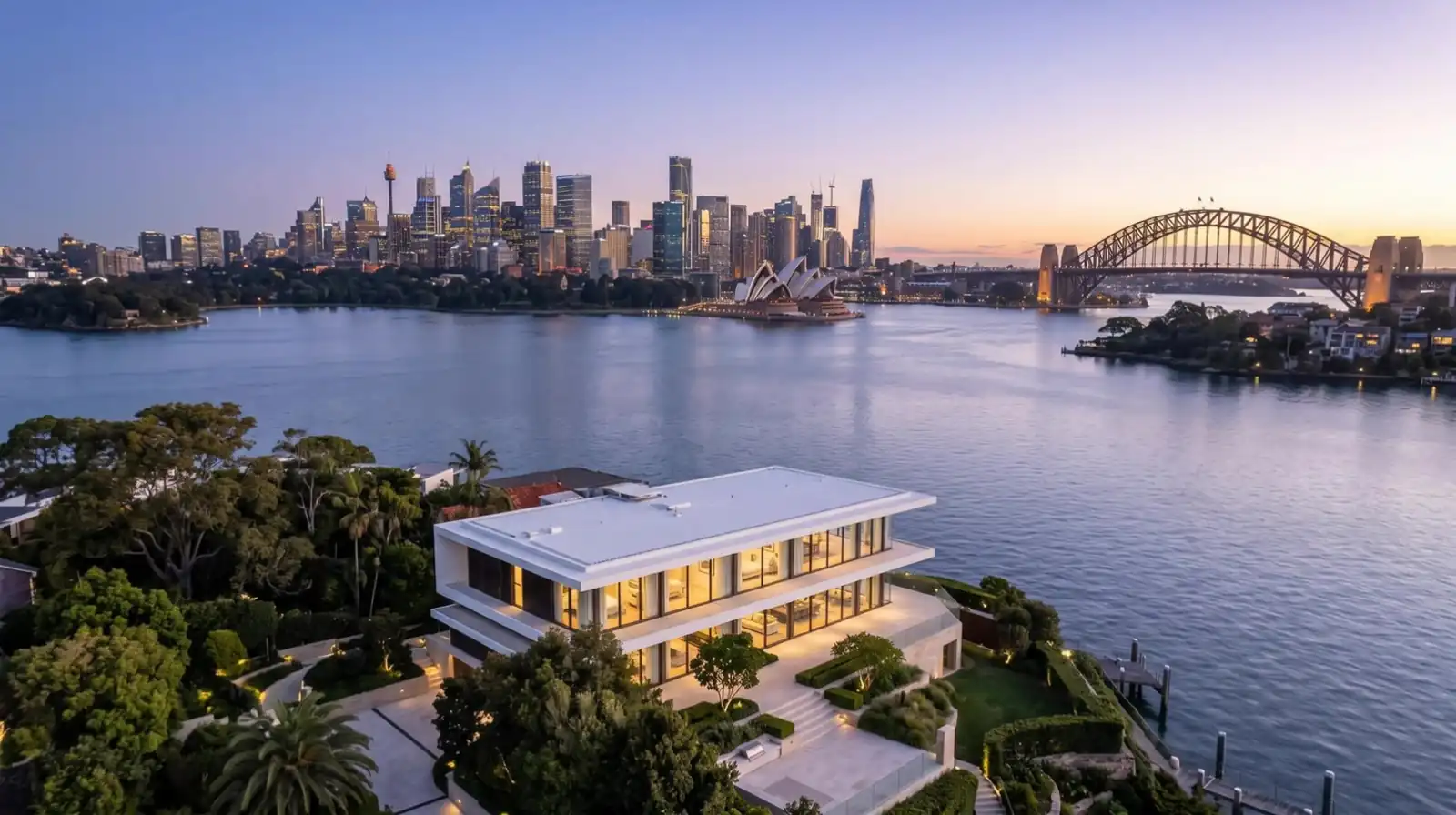 Drone view of a white contemporary harbourside home on Cremorne Point at dusk, looking across Sydney Harbour to the Opera House and Harbour Bridge